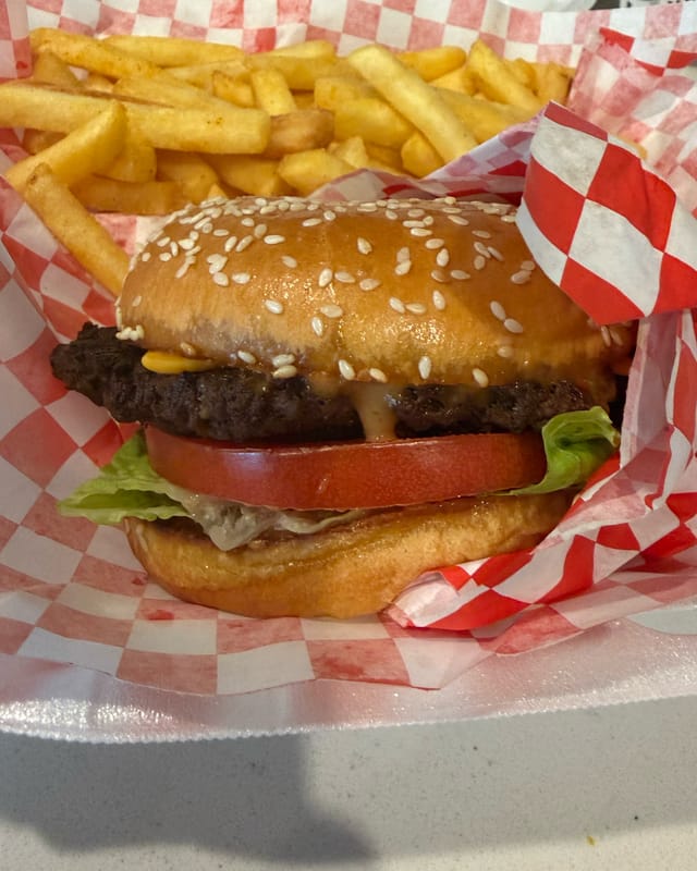 A burger with cheese, lettuce and tomato on a sesame bun, with fries, in a checkered basket