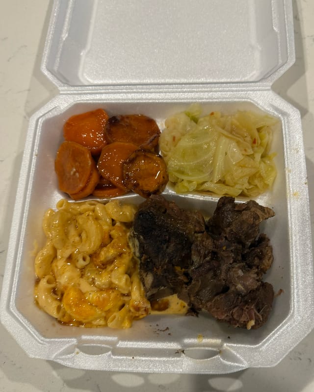 A to-go plate of candied yams, cabbage, macaroni and cheese and braised meat